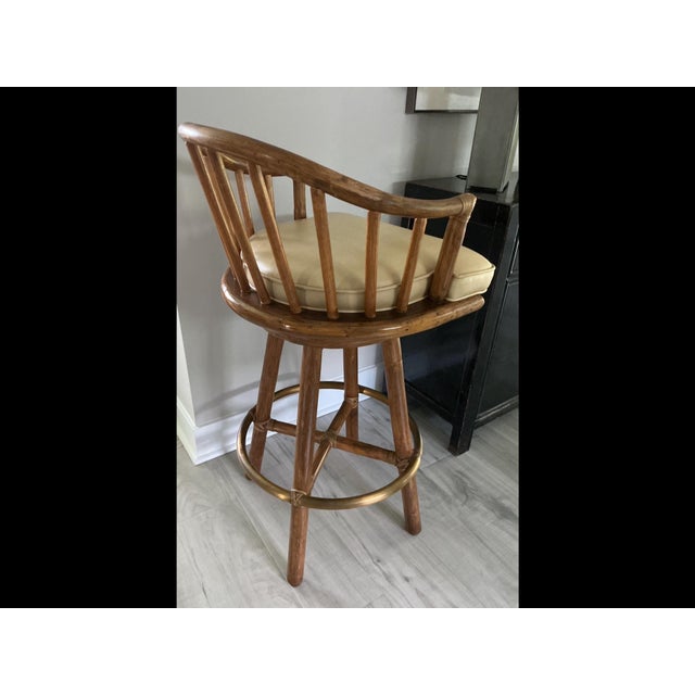 Classic McGuire Barstools. Rattan and Rawhide with tan leather seats Swivel. Brass foot ring. In excellent condition.