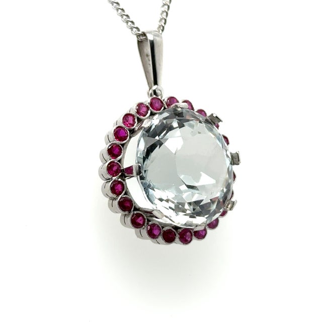A Round Rock Crystal Round Cluster Pendant, claw set in 18ct white gold within a border of 23 round synthetic rubies. Rock...