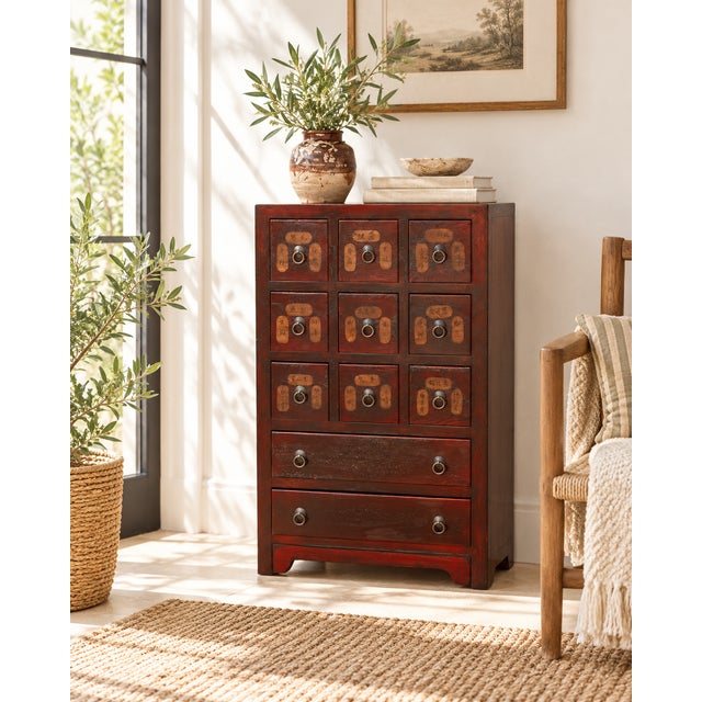 A tall, narrow chest in deep red paint, with eleven drawers that look like a little archive. Nine small drawers sit in a...