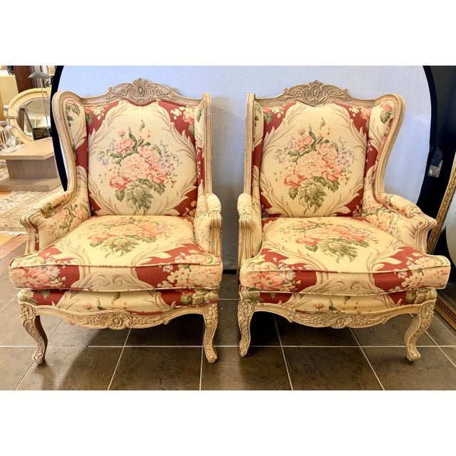 Elegant pair of French Louis XV-style wingback chairs with matching ottomans, featuring carved cabriole legs and softly...