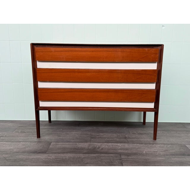 An elegant vintage three-drawer chest of drawers, crafted from teak veneer with white lacquered Formica front details. The...