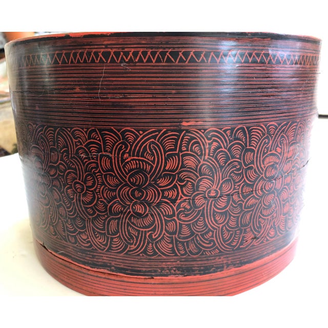 This antique Burmese cylindrical betel-box, 'kun it,' with internal tray is lacquered in red with intricate black accents...