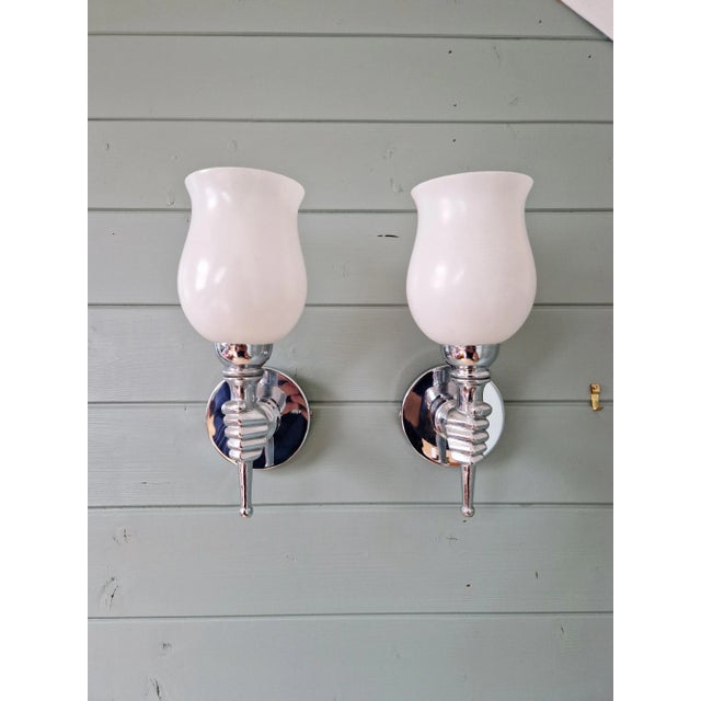 Pair of nickel-plated metal wall sconces depicting a hand holding a torch, with white satin glass, 1960s. Each sconces...