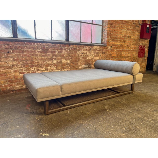 Bright Furniture daybed in grey herringbone upholstery with a cylindrical bolster pillow, raised on a modern bronze-toned...