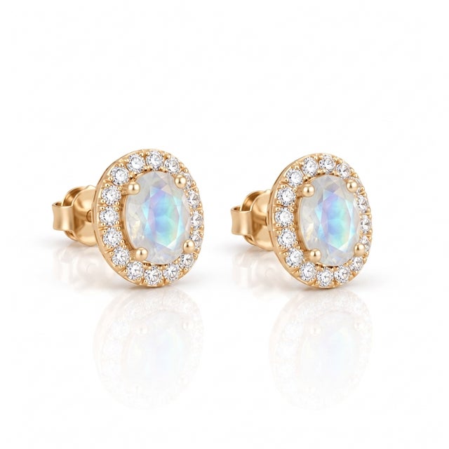 Embrace celestial magic with these alluring rainbow moonstone oval halo stud earrings. Glowing with a soft blue sheen, the...