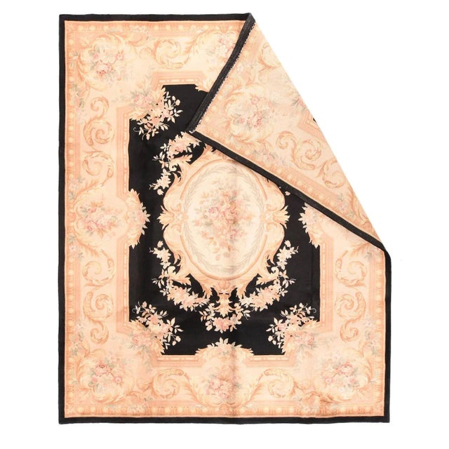 The near black field of this Aubusson-style rug show a cream, elliptical sub-medallion enclosing a floral rose bouquet...