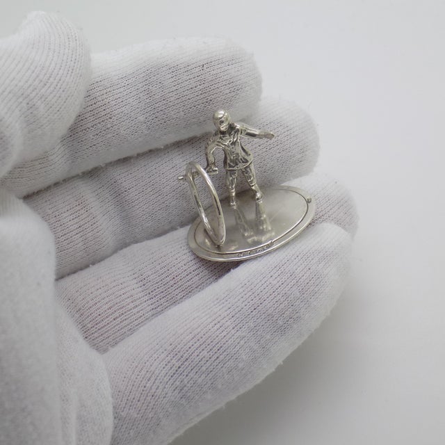A vintage miniature depicting a child playing with a hoop and stick, handcrafted in 835/000 silver in the netherlands in...