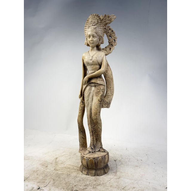 An elegant sculpture depicting a Balinese woman with detailed floral motifs and a majestic headdress, set on a lotus...