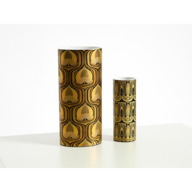 Two beautiful white glazed porcelain vases featuring black and gold geometric shapes resembling abstract peacock feathers....