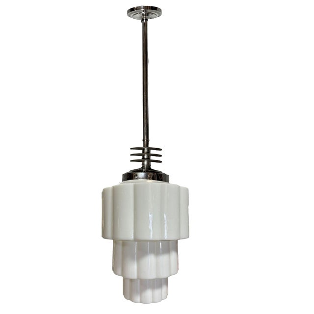This 1930s Art Deco pendant light features a tiered Art Deco milk glass shade featuring stepped geometric layers. It is...