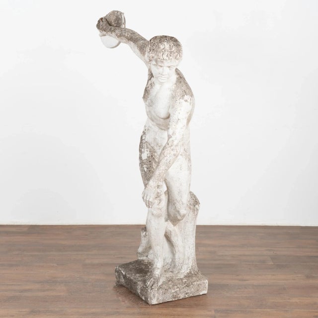 A garden sculpture of discus thrower made of limestone with paint remnants, reminiscent of an ancient Grecian sculpture....