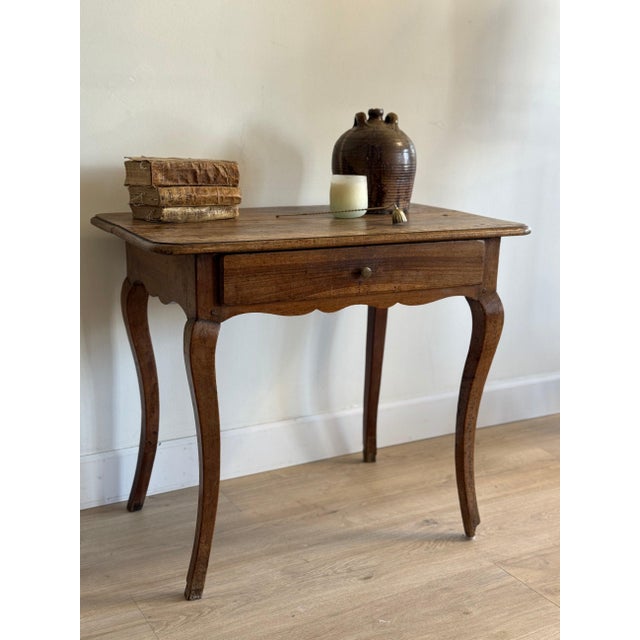 Walnut on slender cabriole legs that splay outward at the toes, the top with rounded corners worn pale where hands rested....