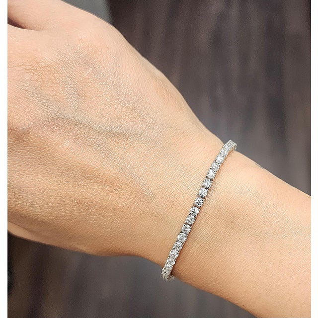 A modern platinum tennis bracelet featuring 55 round white natural diamonds totaling 4.89 carats, graded F/G color and...