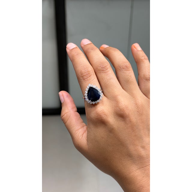 This Blue Sapphire Diamond Halo Ring showcases a 8.42-carat natural deep blue sapphire, set in 18k white gold. The Blue...