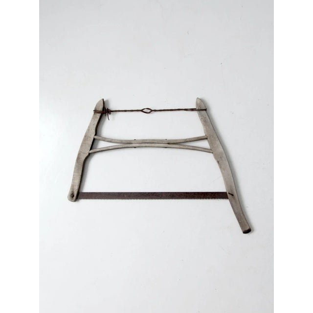 This is an antique buck saw. The primitive tool features a wood frame with metal saw blades and cross-wire hardware.