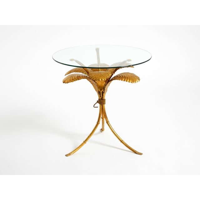 Rare 1960s gilt Florentine side table or nightstand. The frame features three curved legs topped with a thick, round glass...