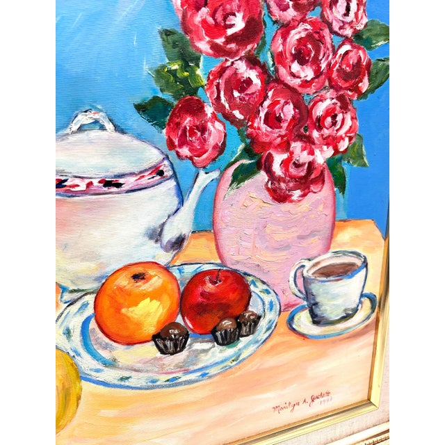Colorful signed floral still life painted by Marilyn A. Juckett and dated 1993, depicting red flowers, fruit, teacup and...
