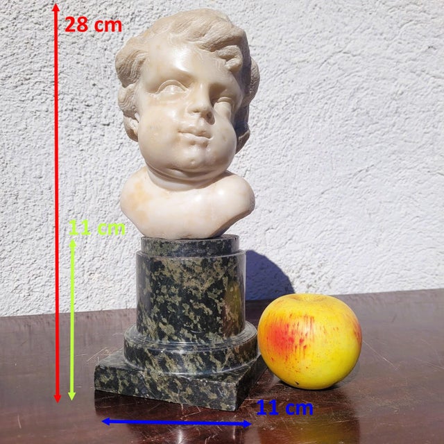 Beautiful white marble putto head mounted on a green marble column: this chubby putto is depicted in the purest Baroque...