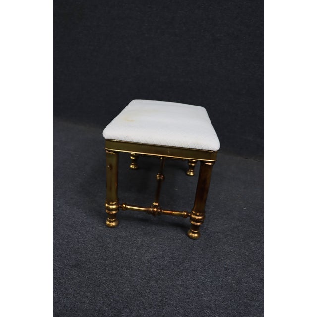 Classic Hollywood Regency gilt footstool with turned legs and decorative stretchers. Finished in a warm gilt tone with an...