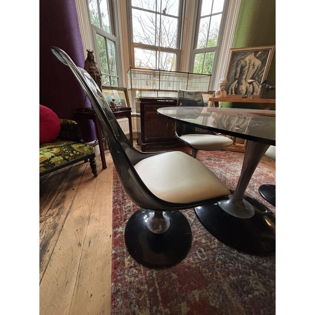 The dining set consists of a smoked glass oval table on a pedestal base accompanied by 4 swivel chairs on pedestal bases...