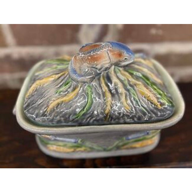 A majolica lidded game dish of earthenware decorated with a high gloss glaze and a three dimensional figural fish on a...