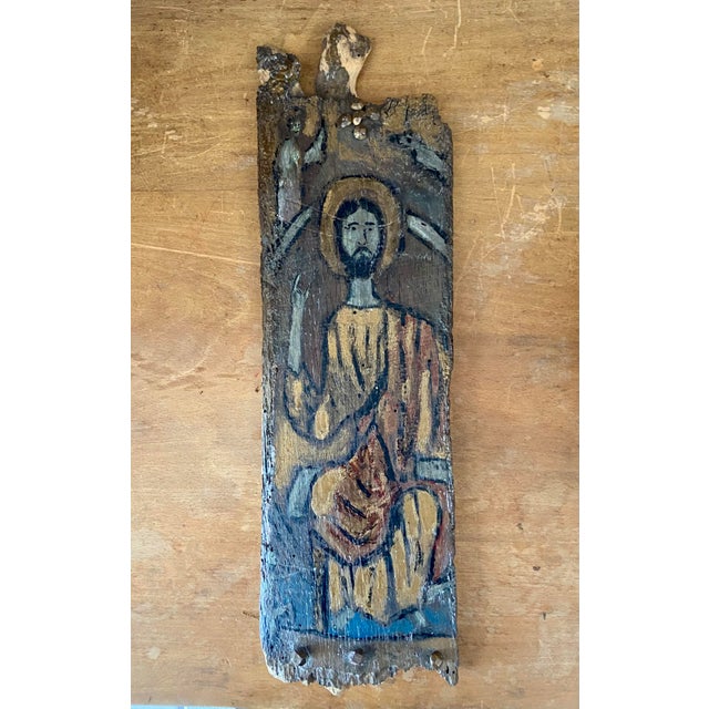 A striking primitive devotional panel, hand-painted on a naturally weathered wooden plank, likely dating from the early...