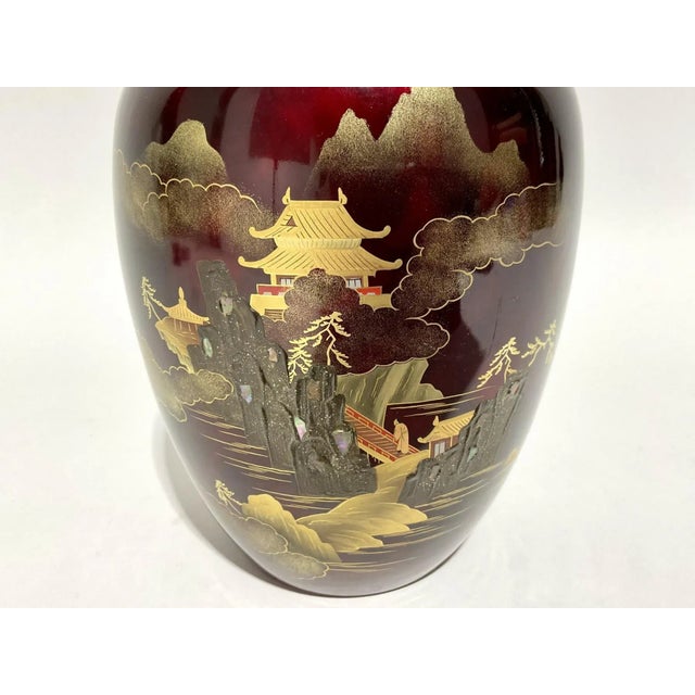 With tapered form and textured landscape scene with gold accents on a cabernet glaze. It is marked on underside.