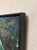 The painting depicts a serene figure in a green garment, seated at a round table, exuding a sense of calm and...