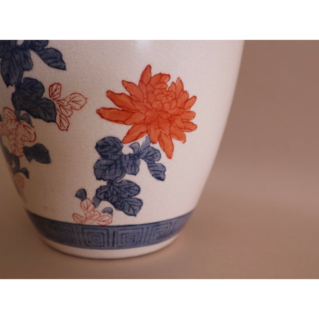 Hand-painted vase from China with orange and blue floral motif. Crackle cream glaze backdrop. Blue painted border at...