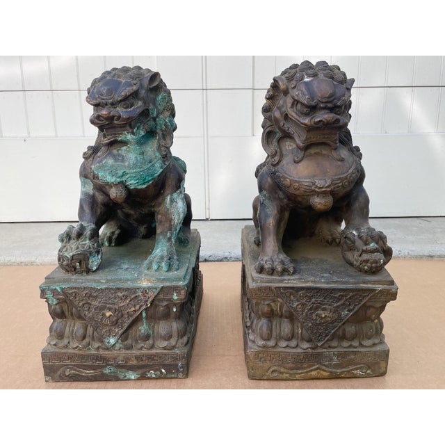 A pair of antique guardian lions or foo dogs in cast bronze. They have aged beautifully, accruing a rich patina with some...
