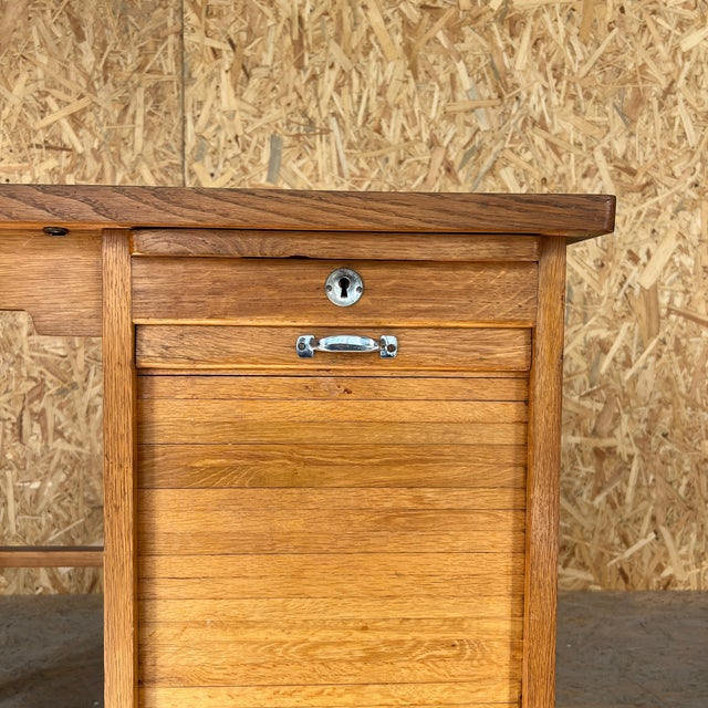 1920s small compact French tambour desk featuring a warm, honey-toned natural wood finish. The piece is designed with a...