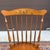A pair of vintage L. Hitchcock Traditional solid maple comb back Windsor dining chairs with having gold stenciling on the...