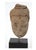 A small carved and weathered sandstone Buddha head in tan-brown tones with darker mineral staining, downcast, meditative...