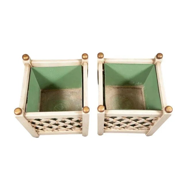 A pair of painted wood square planters with a diagonal lattice motif on each side revealing a green plant insert to hold a...