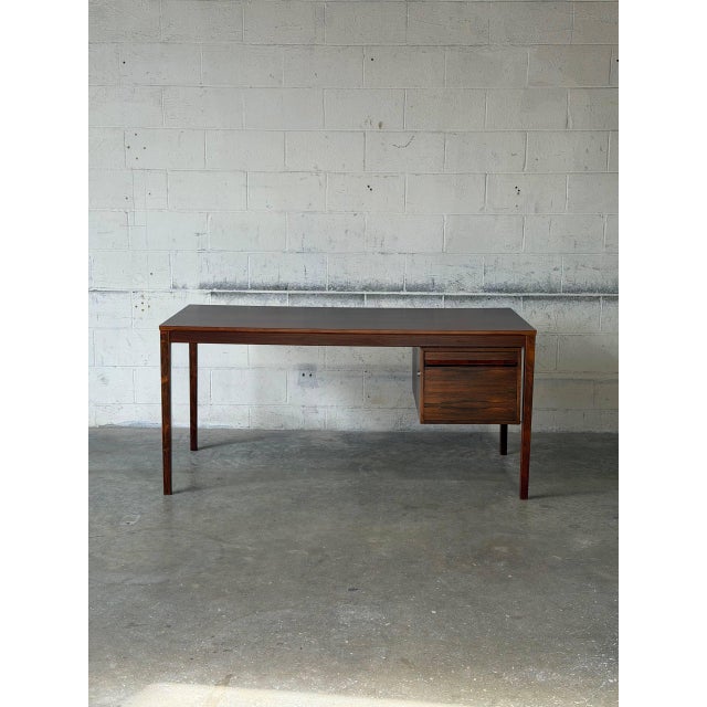 This striking desk features a broad rectangular top and an asymmetrical profile defined by a deep drawer unit. The design...