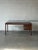 This striking desk features a broad rectangular top and an asymmetrical profile defined by a deep drawer unit. The design...