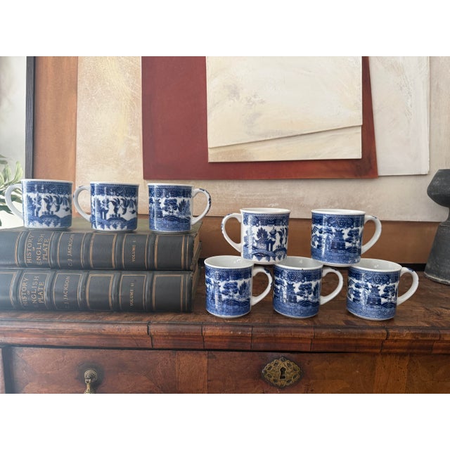Set of eight blue willow coffee mugs featuring a rich, inky cobalt transferware design on glossy white ceramic. The...