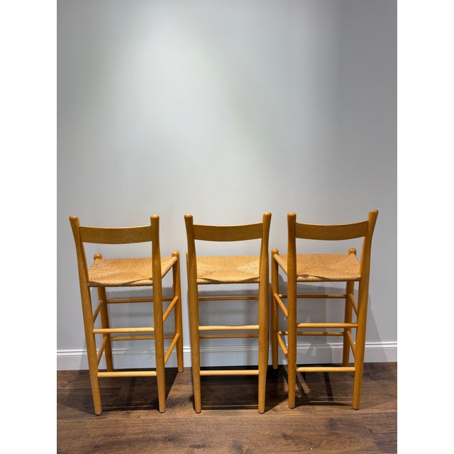 A beautifully crafted set of three Danish Modern style bar stools featuring solid oak frames and handwoven rush seats in...