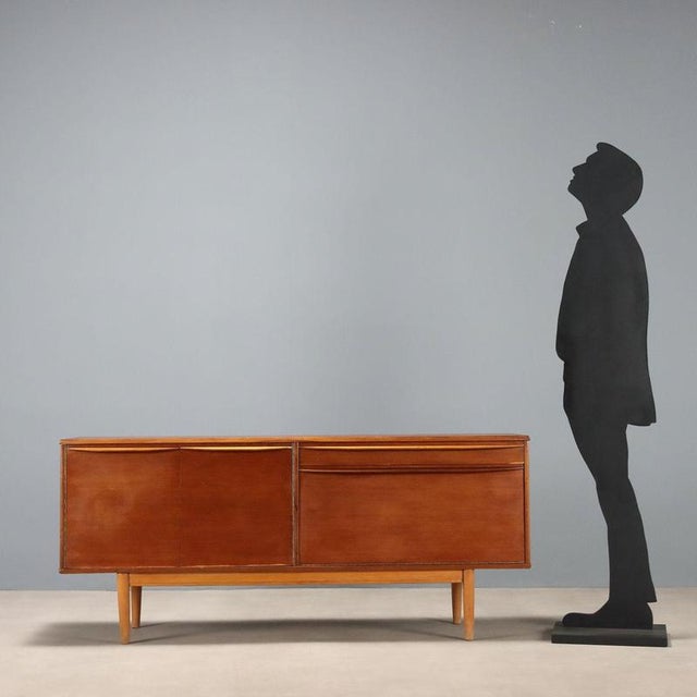 Sideboard with hinged doors, flap and under-counter drawer, in teak veneer. This piece is attributed to the mentioned...