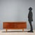 Sideboard with hinged doors, flap and under-counter drawer, in teak veneer. This piece is attributed to the mentioned...
