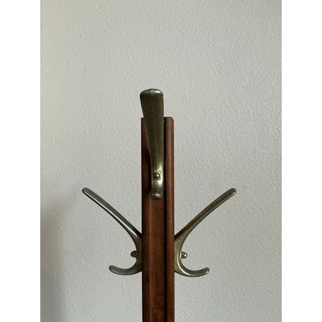 A clean, minimalist solid‑wood coat rack featuring a tall turned post, two metal double hooks, and a sturdy cross‑base....