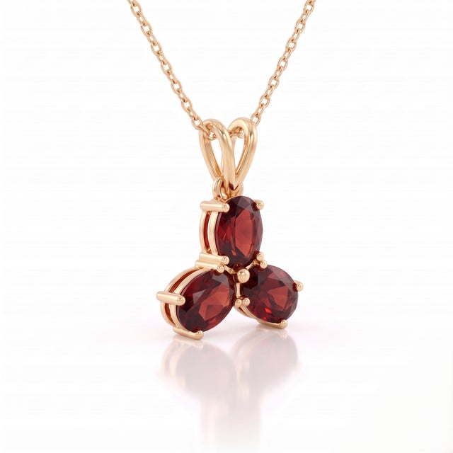 A striking three-stone design featuring oval-cut natural garnets arranged in a graceful trefoil formation, secured in a...
