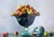 Multicolored apples fill an elegant crystal vase collocated on a smooth surface. This vase is the heart of the composition...