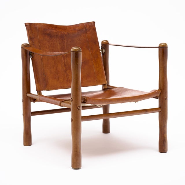 A handsome mid-century safari-style armchair combining a warm wood frame with beautifully aged cognac leather. The chair...