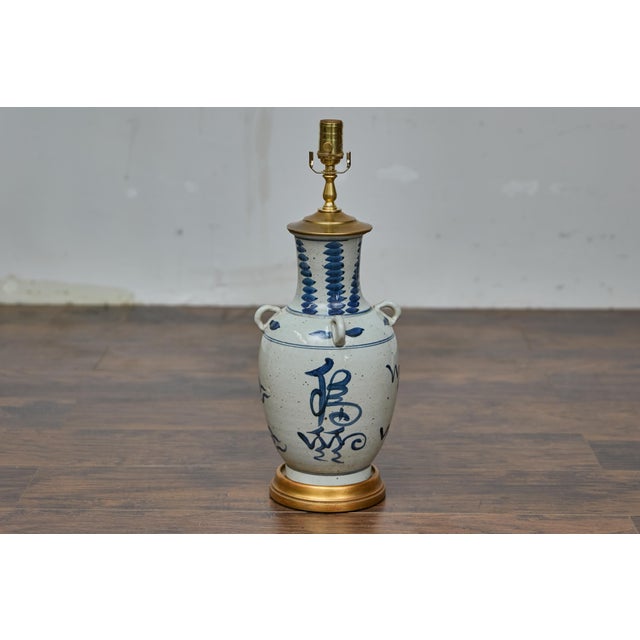 An Asian porcelain vessel table lamp with custom gilt wooden base, wired for the USA. This striking table lamp, crafted...