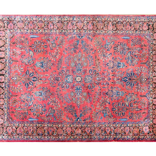 A very traditional early 20th century Persian Sarouk rug with a mirrored floral pattern of large floral clusters woven in...