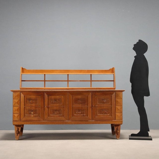 Buffet with raised top, with swing doors, in oak veneer, decorative carved panels. This piece is attributed to the...