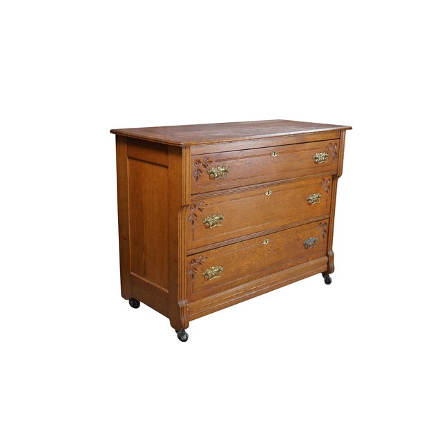 This antique Late Victorian oak dresser features three stacked, full-width drawers framed by elegant hand-carved floral...