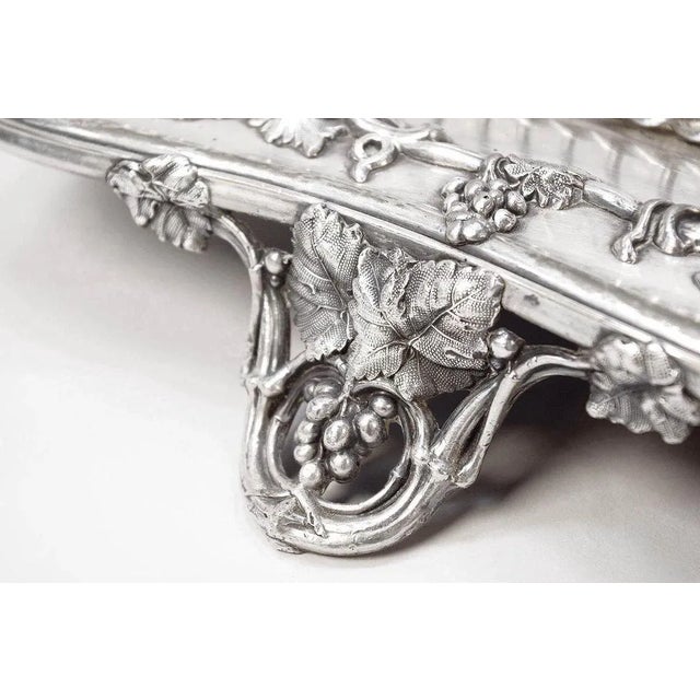 Silver-plated metal centrepiece with a curve-shaped plate adorned with a vine branches frieze on the edge, standing on...