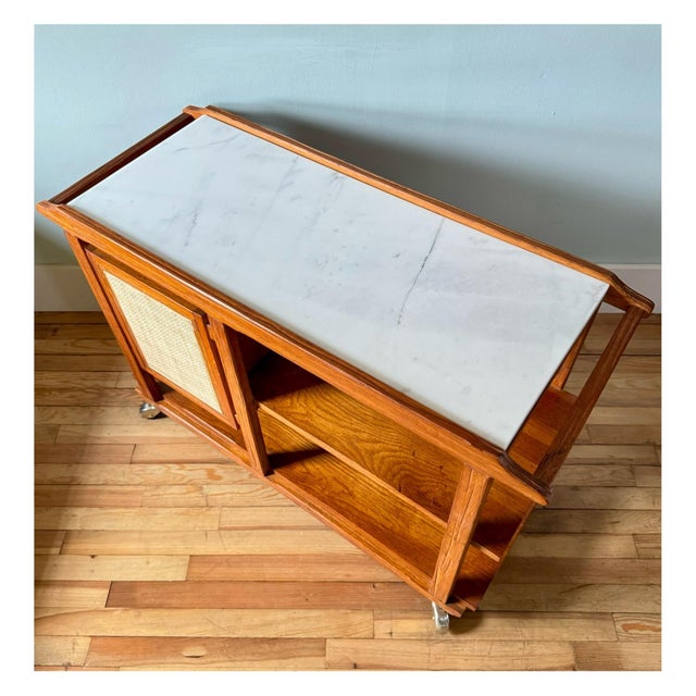 Handsome mid century barcart features new white marble top and caned webbing. Two lower shelves and enclosed cabinet with...